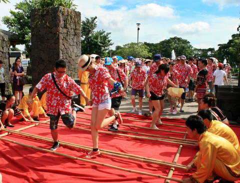 在大门口，爱侣穿着红色休闲装，牵着手、伴着音乐、跳着黎族竹竿舞步入公园